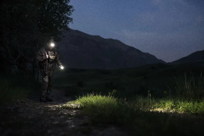 Hunter hiking in the dark with a flashlight and headlamp lighting the path.