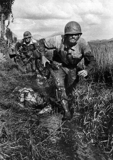 Two US Marines make a running advance along a muddy ditch somewhere in Korea. The trailing Marine is carrying a Browning Automatic Rifle.