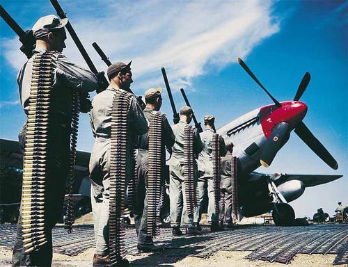 US Army Air Forces armorers bring a half dozen .50 caliber Brownings and numerous belts of ammo out to the flight line to arm a P-51 Mustang during WWII.