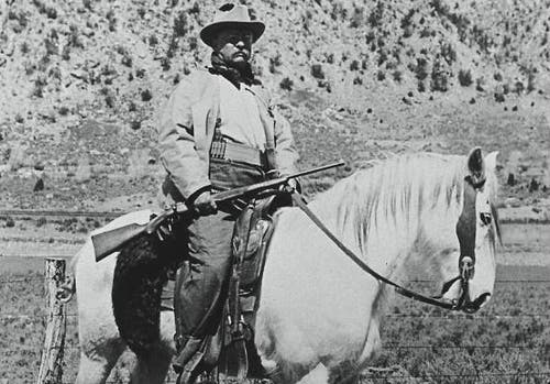 Theodore Roosevelt on a white horse with a bolt action rifle.
