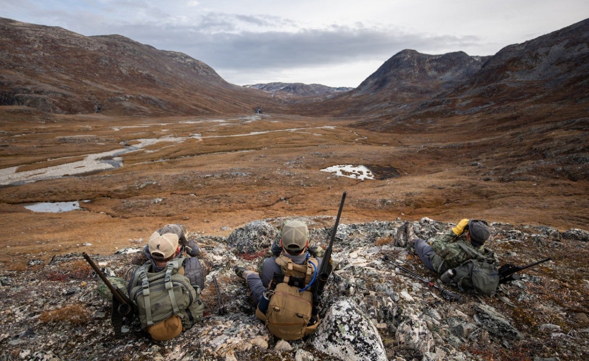 Three hunters with packs sitting on rocks glassing.